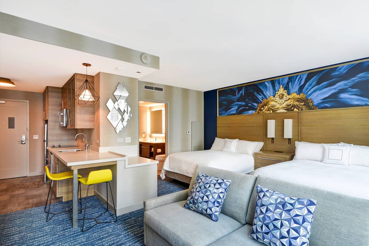 A hotel room with a bed, a sofa, a desk with a chair, a bathroom, and a large window.