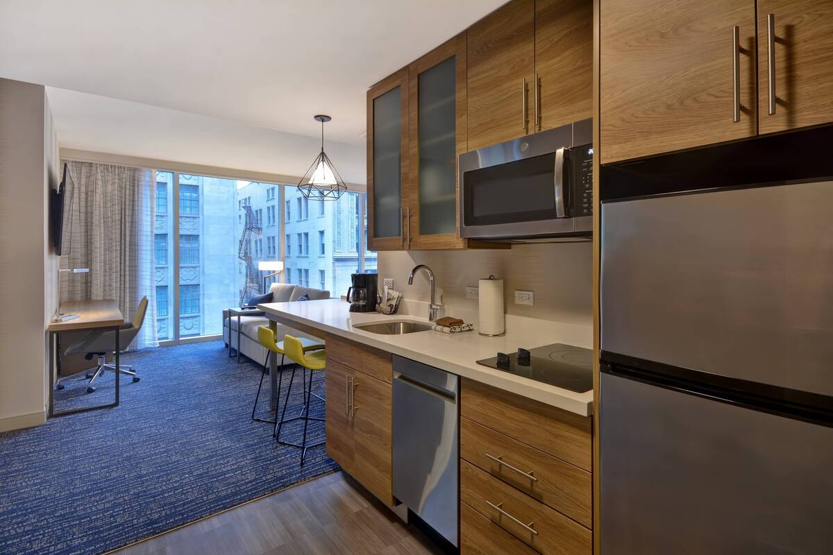 A modern kitchen with wooden cabinets, stainless steel appliances, and a large window overlooking a cityscape.