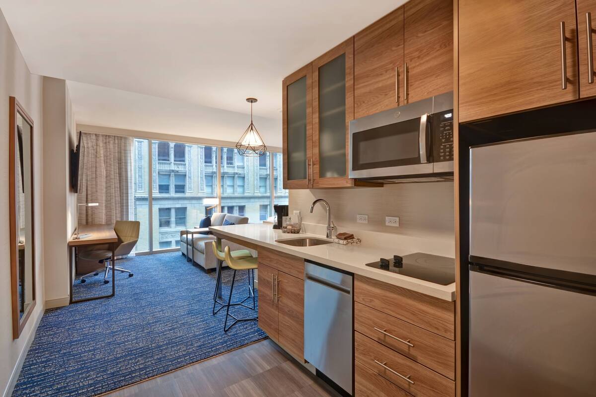 A modern kitchen with wooden cabinets, stainless steel appliances, and a large window offering a city view.