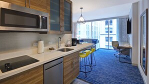 A modern kitchen with a stainless steel microwave, wooden cabinets, and a built-in dishwasher. There is a bar area with yellow stools and a seating area with a desk and chair. - Residence Inn by Marriott New Orleans French Quarter Area/Central Business District (New Orleans)