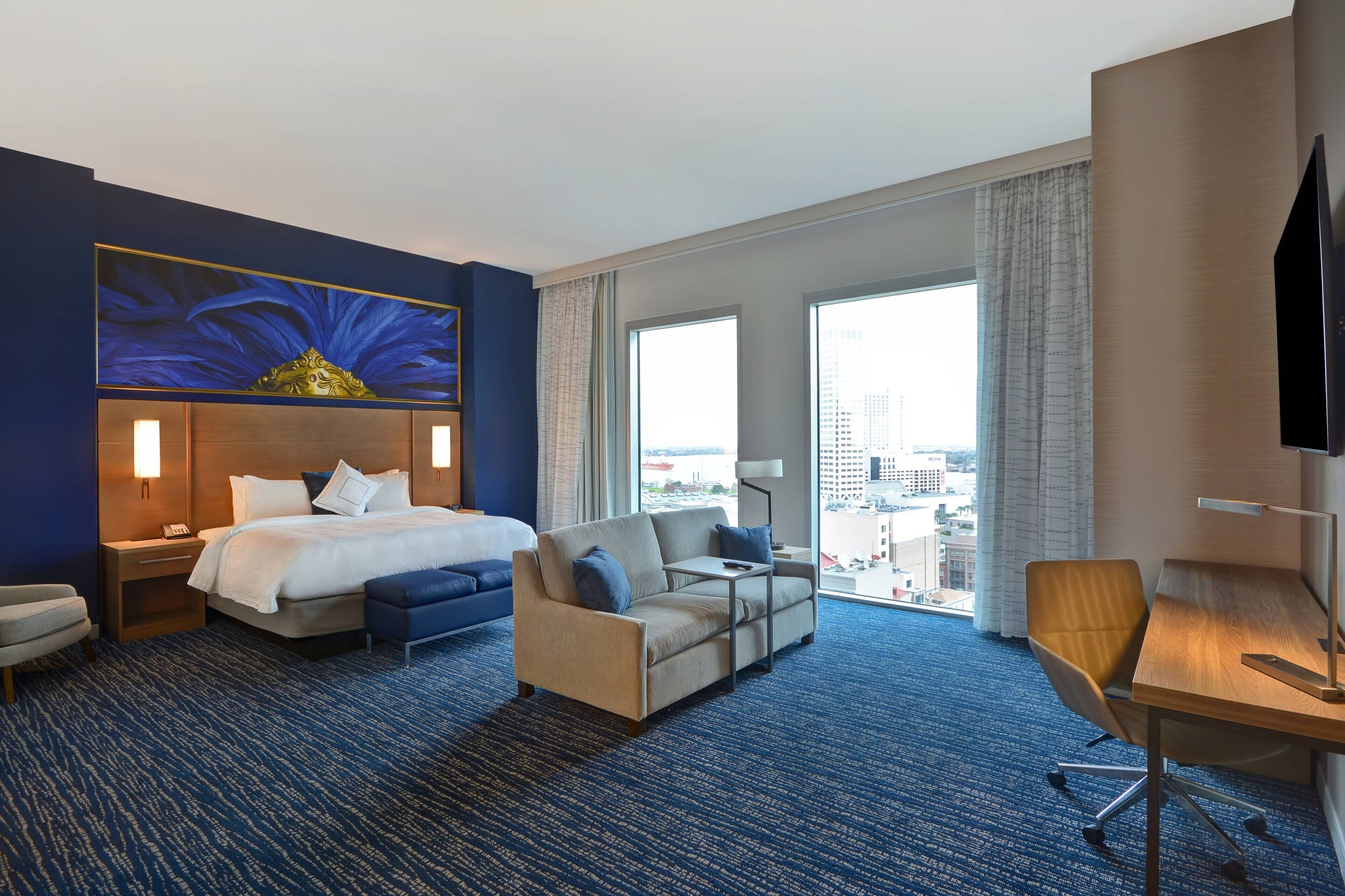 Habitación de hotel con cama, sofá, escritorio y un amplio ventanal con vistas a la ciudad.