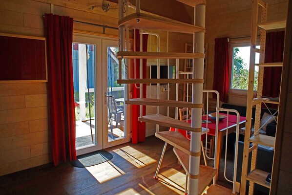 A room with a wooden floor, a red curtain, a white chair, a red table, and a window with a view of the outside.
