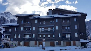 Un hotel de varios pisos con balcones, un cartel de estación de esquí y alrededores nevados.
