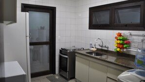 A compact kitchen with white tiles, a gas stove, a sink, and a window above the countertop. - Beautiful Townhouse in Lázaro Beach - Ubatuba (Ubatuba)