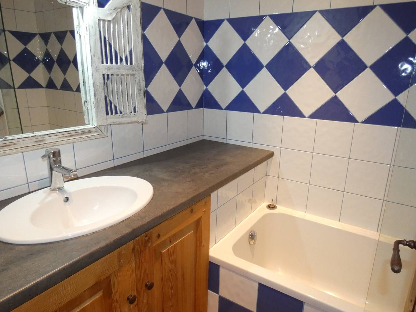 A bathroom with a white sink, a wooden cabinet, a mirror, and a bathtub with a white tiled wall.
