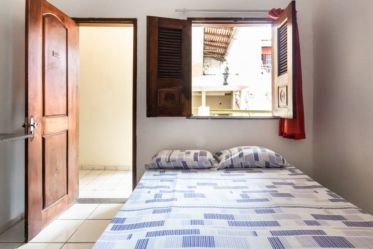 Um quarto com uma cama, uma janela com persianas e uma porta.