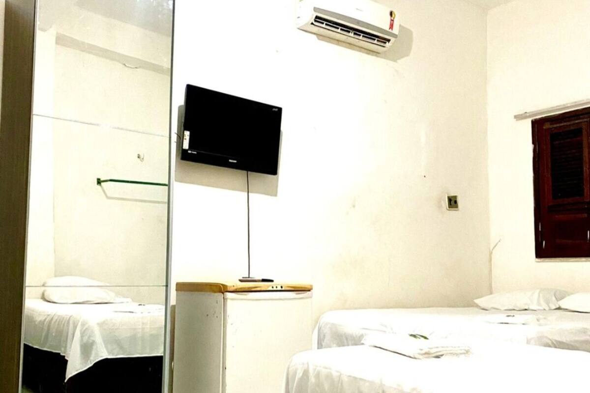 Quarto de hotel com duas camas, uma televisão de tela plana na parede e um aparelho de ar condicionado.