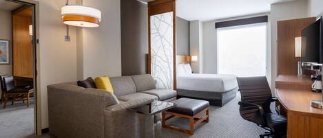 A hotel room with a sofa, a small table, a desk, a chair, a bed, and a TV.