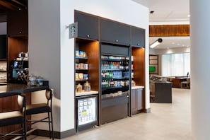 Un moderno vestíbulo de hotel con mostrador Starbucks, exhibición refrigerada de bebidas y zona de estar.