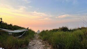 A pathway leading to a beach with a hammock and a chair. - BEACH Front w/ HOT TUB🔥 Mid Century Home! (Norfolk)
