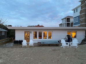 A coastal house with a covered patio, white Adirondack chairs, and a swing chair.