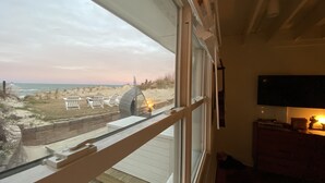 A room with a large window overlooking a beach with beach chairs and a dune buggy. - BEACH Front w/ HOT TUB🔥 Mid Century Home! (Norfolk)
