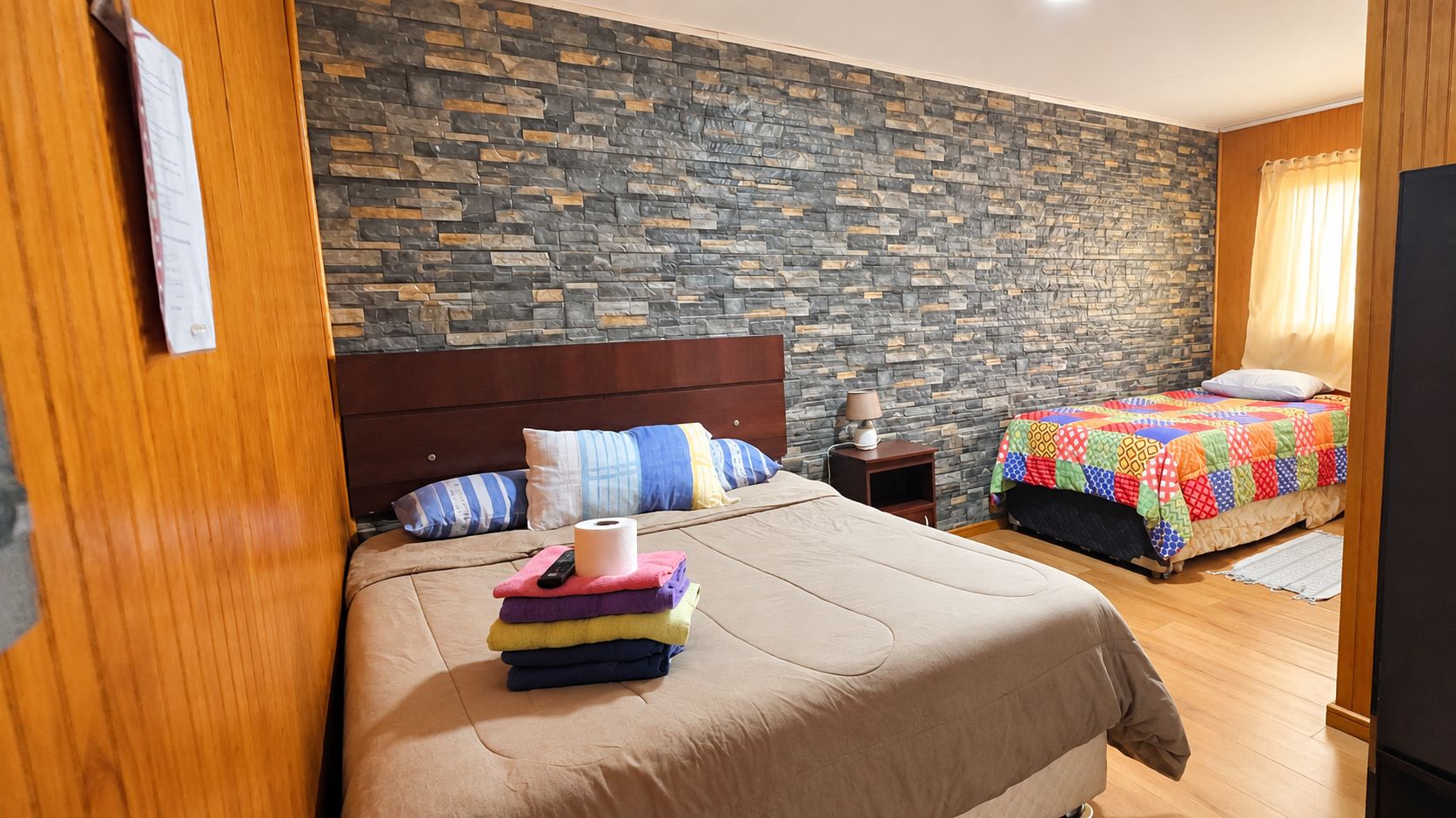 A hotel room with a large bed, a smaller bed, a nightstand, and a stone-patterned wall.
