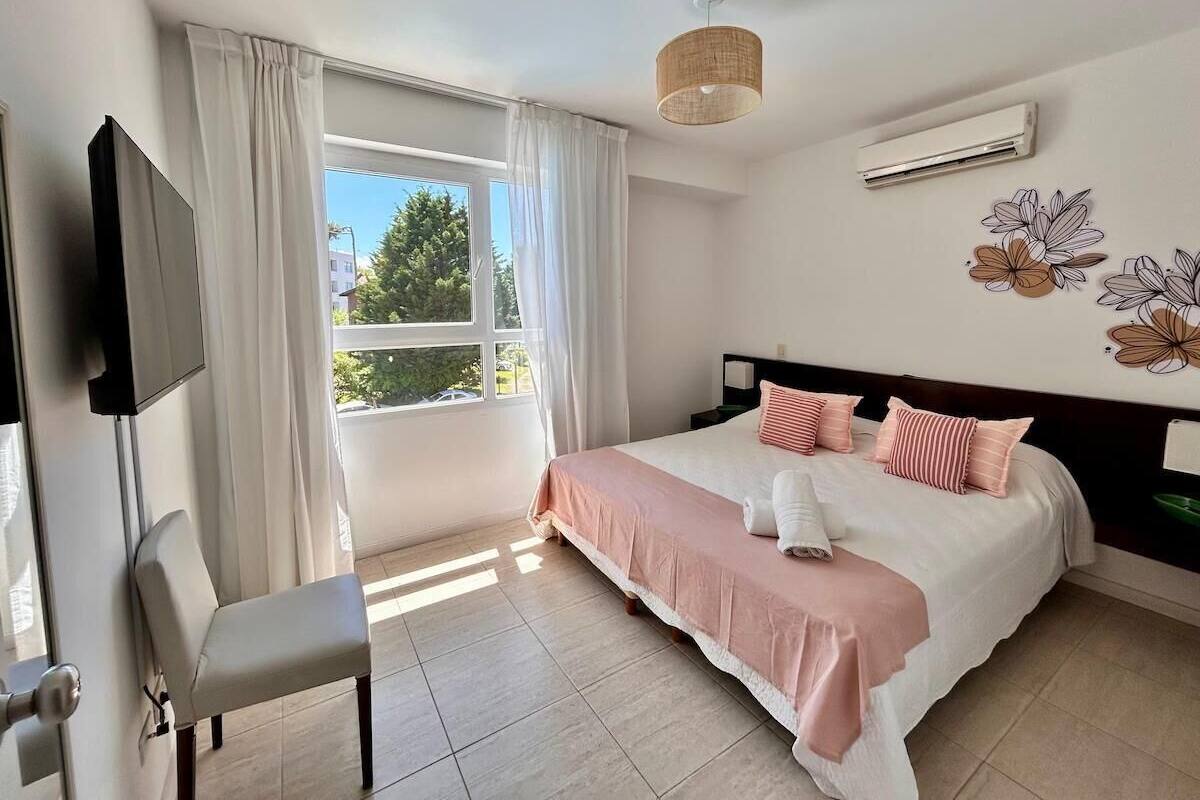 A hotel room with a bed, a chair, a TV, and a window with curtains.