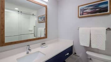 Un baño con un lavabo blanco, un espejo con marco de madera, un inodoro y un perchero con dos toallas.