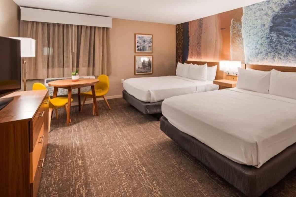 A hotel room with two beds, a desk, a chair, and a painting on the wall.