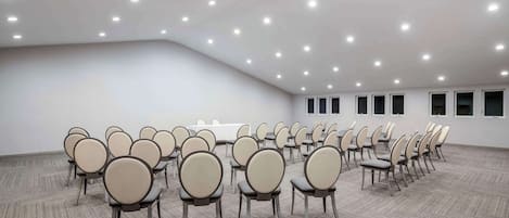 A conference room with rows of chairs, a white table, and a carpeted floor.