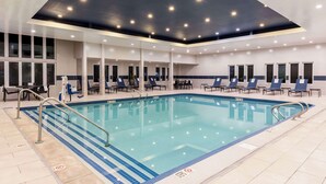 Una piscina con solárium azulejado, sillas de descanso e iluminación empotrada en el techo.