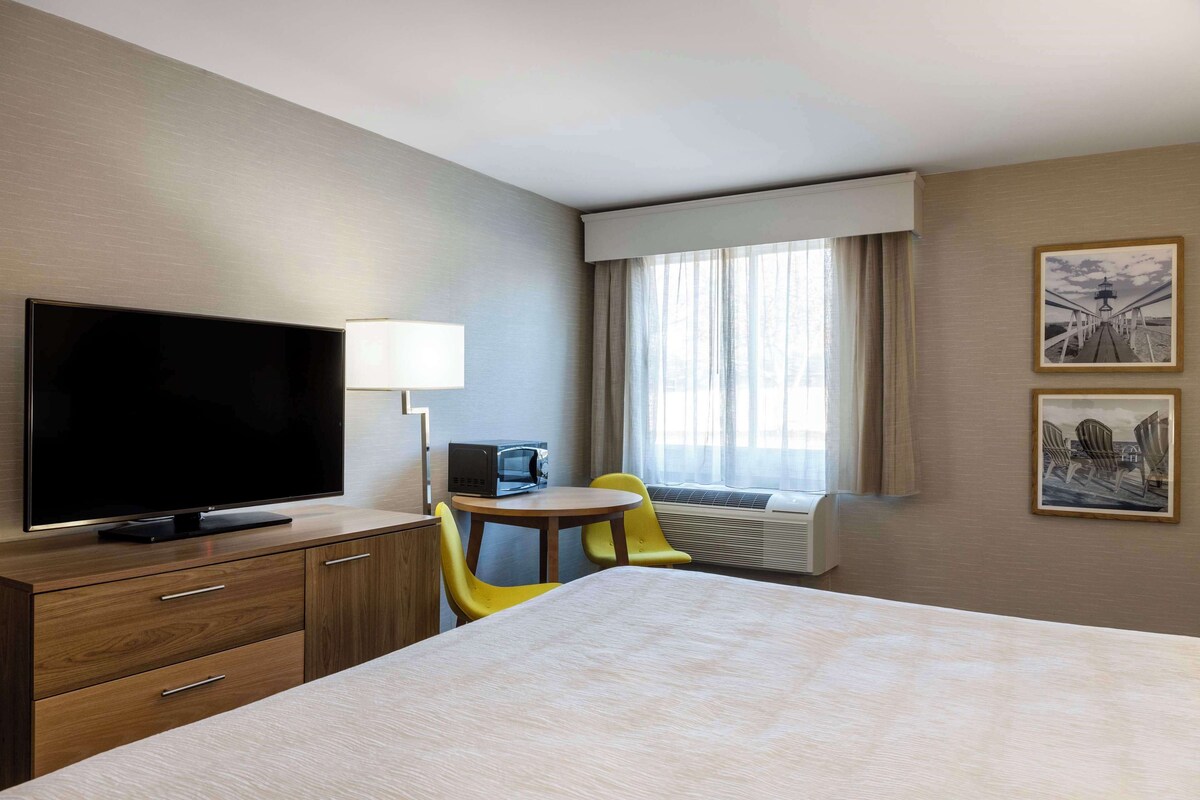 A hotel room with a bed, a TV, a desk with a lamp, a chair, and a window with curtains.