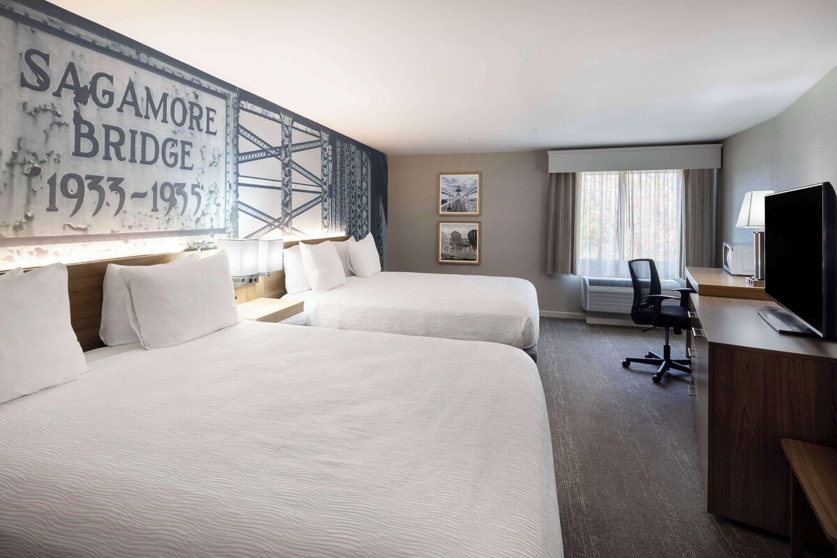 A hotel room with two beds, a desk with a TV, and a large wall mural.
