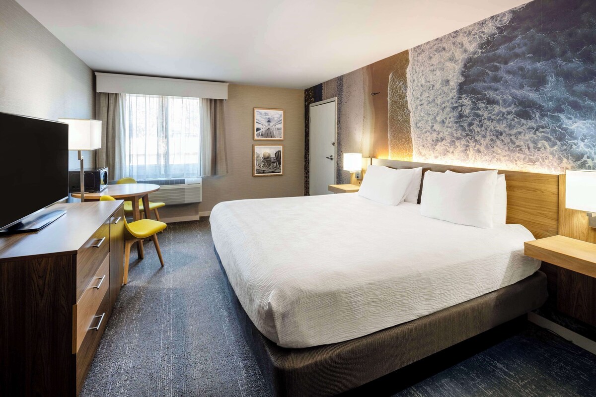 A hotel room with a large bed, a desk with a chair, a television, and artwork on the walls.