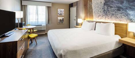 A hotel room with a large bed, a desk with a chair, a television, and artwork on the walls.
