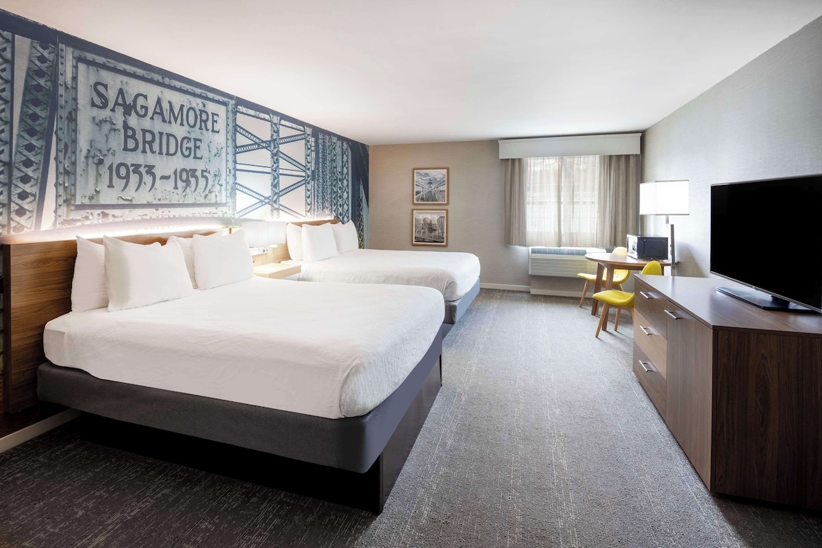 Ein Hotelzimmer mit zwei Betten, einem Schreibtisch mit Stuhl, einem Fernseher und einem großen Wandbild.