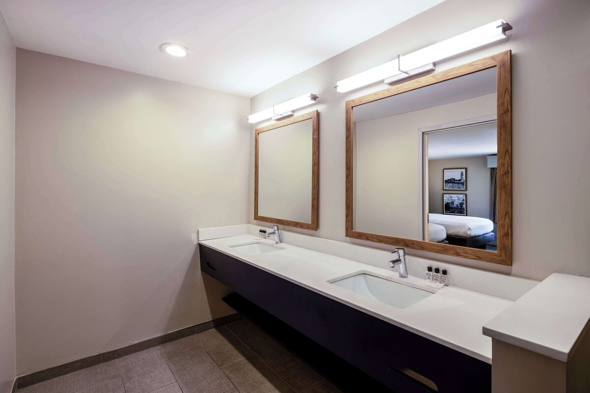 A modern bathroom with two sinks, large mirrors, and overhead lighting.