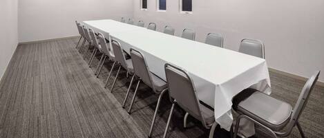 Un salón de conferencias con una larga mesa, sillas grises, suelo alfombrado y luces empotradas en el techo.