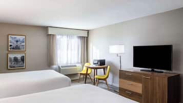 A hotel room with two beds, a desk with a TV, a lamp, and two chairs.