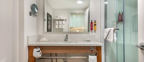 A modern bathroom with a glass shower enclosure, a large mirror, and a wooden vanity with a towel rack.