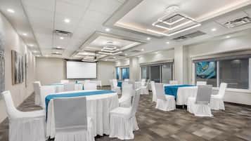A conference room with white chairs and tables, a projector screen, and a large window.