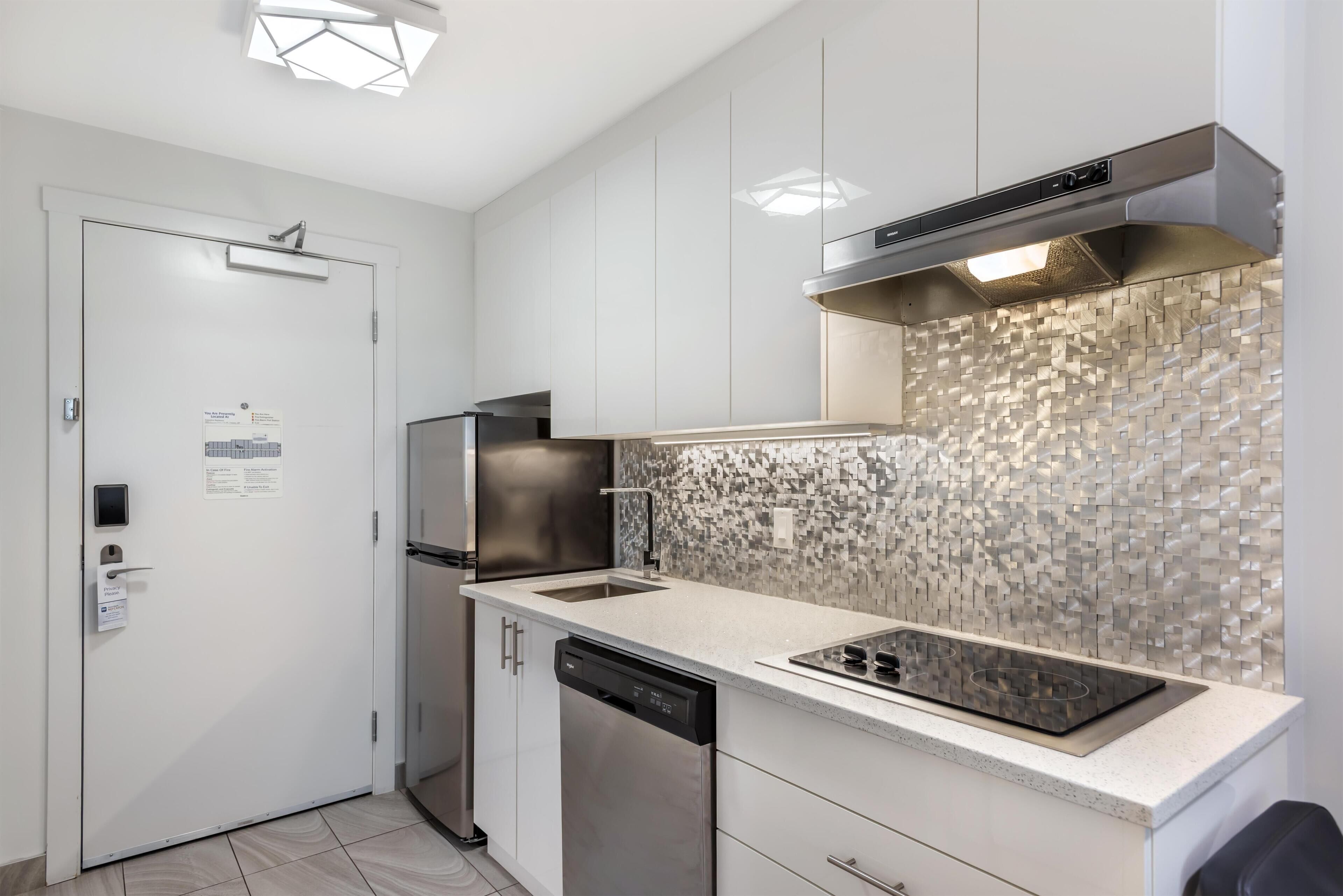 Una cocina moderna con armarios blancos, un refrigerador de acero inoxidable, un lavavajillas y un salpicadero azulejado.