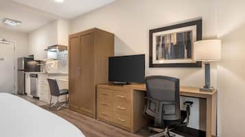 A hotel room with a bed, a desk with a chair, a television, a wardrobe, and a painting on the wall.