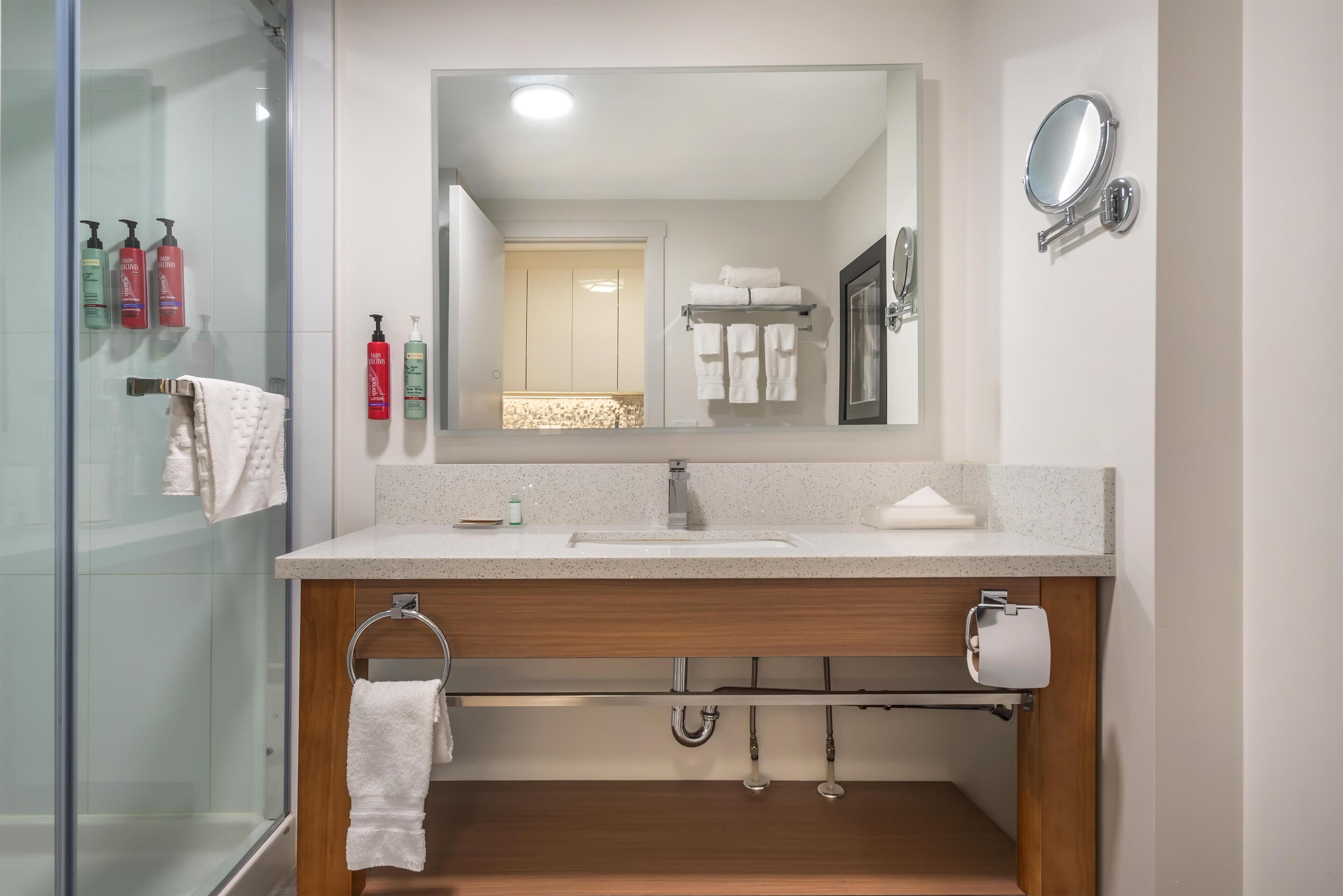 Ein modernes Badezimmer mit Duschkabine aus Glas, Holzwaschtisch, großem Spiegel und Handtuchhalter.