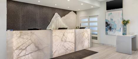 A reception desk with a marble design, a mounted flat-screen TV, and a modern interior.