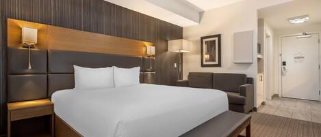 Una habitación de hotel moderna con una cama grande, mesitas de noche, un banco y una zona de estar.