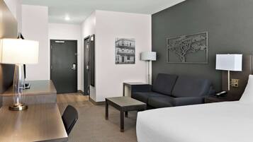 A hotel room with a bed, a desk, a chair, a sofa, a small table, and a lamp.