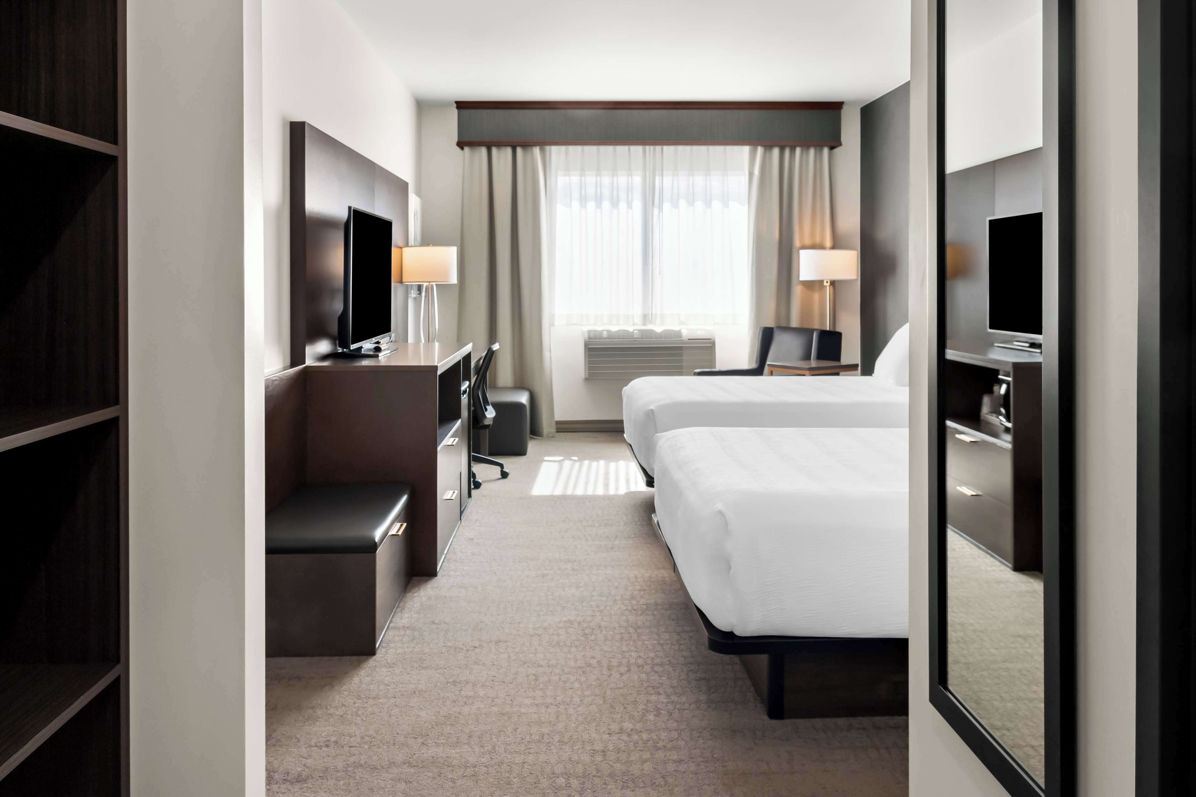 A hotel room with a bed, a desk, a chair, a TV, and a large mirror.
