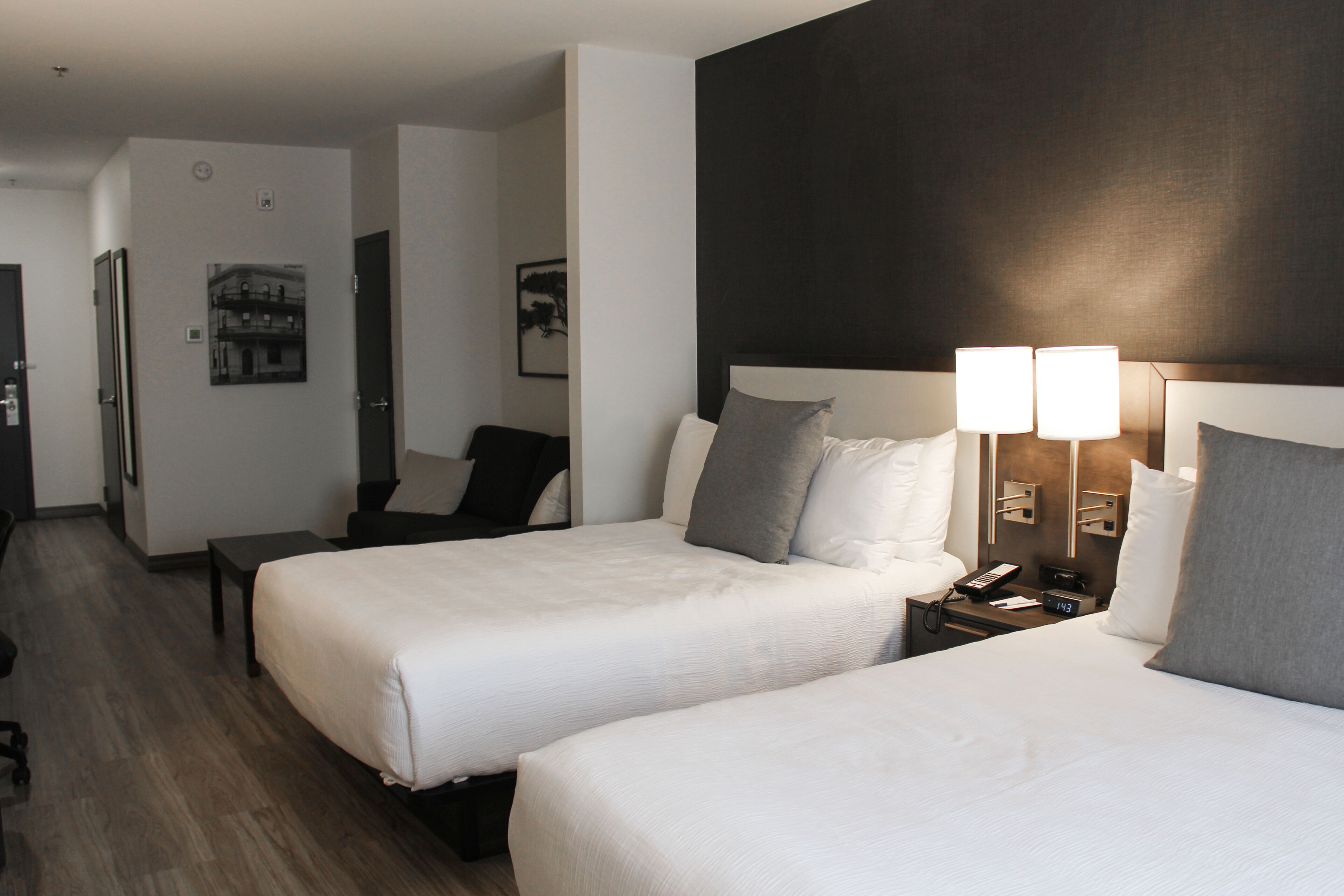 Een hotelkamer met twee bedden, een bureau en een stoel. Er is een nachtkastje met een lamp en een telefoon.