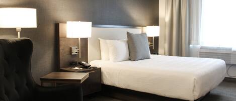 A hotel room with a large bed, two bedside tables with lamps, a chair, and a window with curtains.