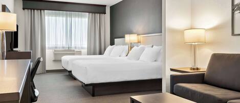 Una habitación de hotel con una cama grande, dos mesitas de noche con lámparas, un sofá, un escritorio y una silla.