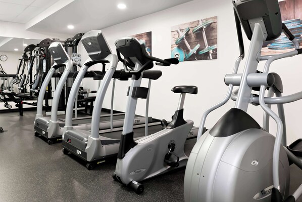 Une rangée de vélos d’appartement dans une salle de sport, avec une horloge au mur.