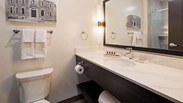 A bathroom with a toilet, a sink with a mirror, and towels on towel racks.