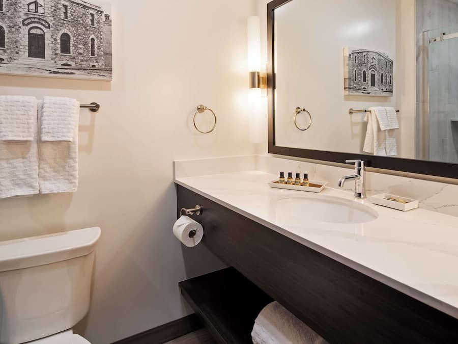 A bathroom with a toilet, a sink with a mirror, and towels on towel racks.