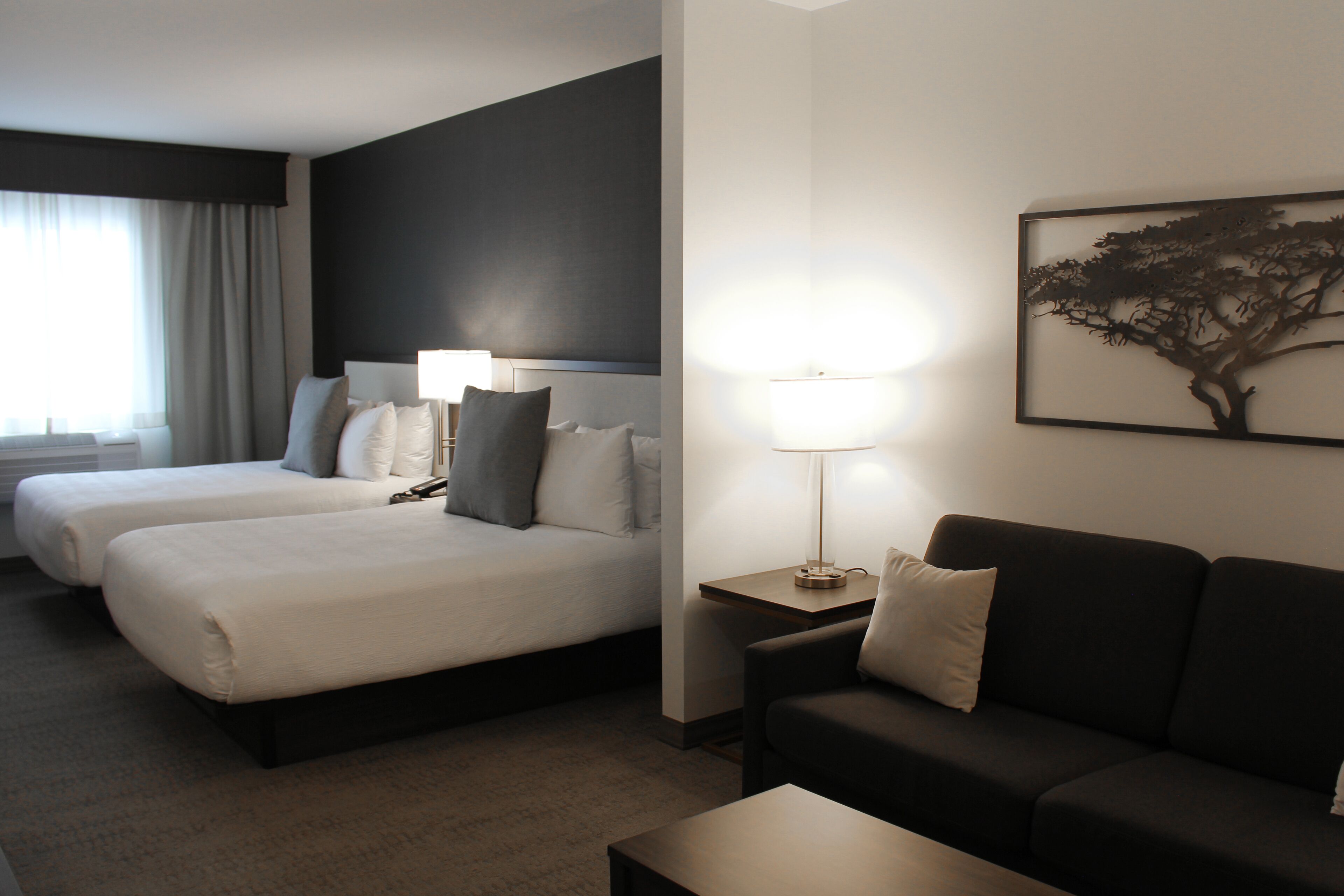 Ein Hotelzimmer mit zwei Betten, einem Schlafsofa, einer Lampe und einem gerahmten Bild an der Wand.