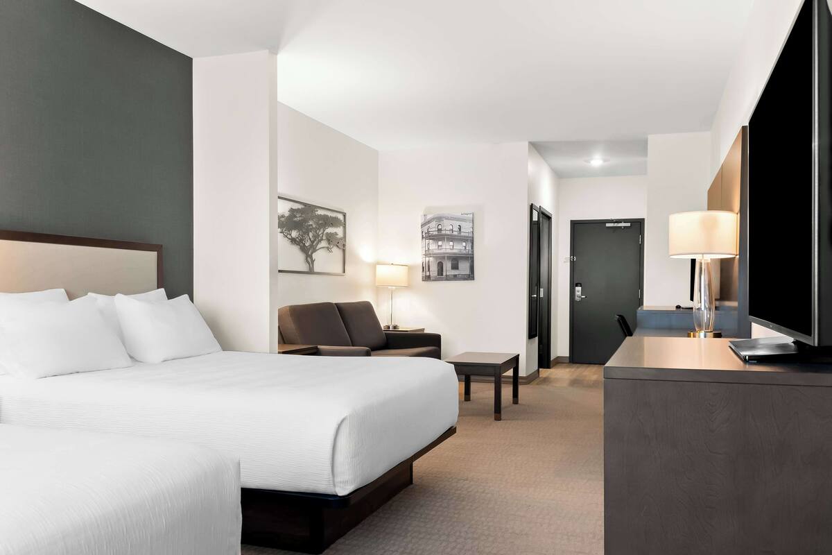A hotel room with a large bed, a desk, a chair, a lamp, and a door.