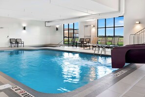 An indoor swimming pool with clear water, a tiled floor, and a view of the outdoors through large windows.