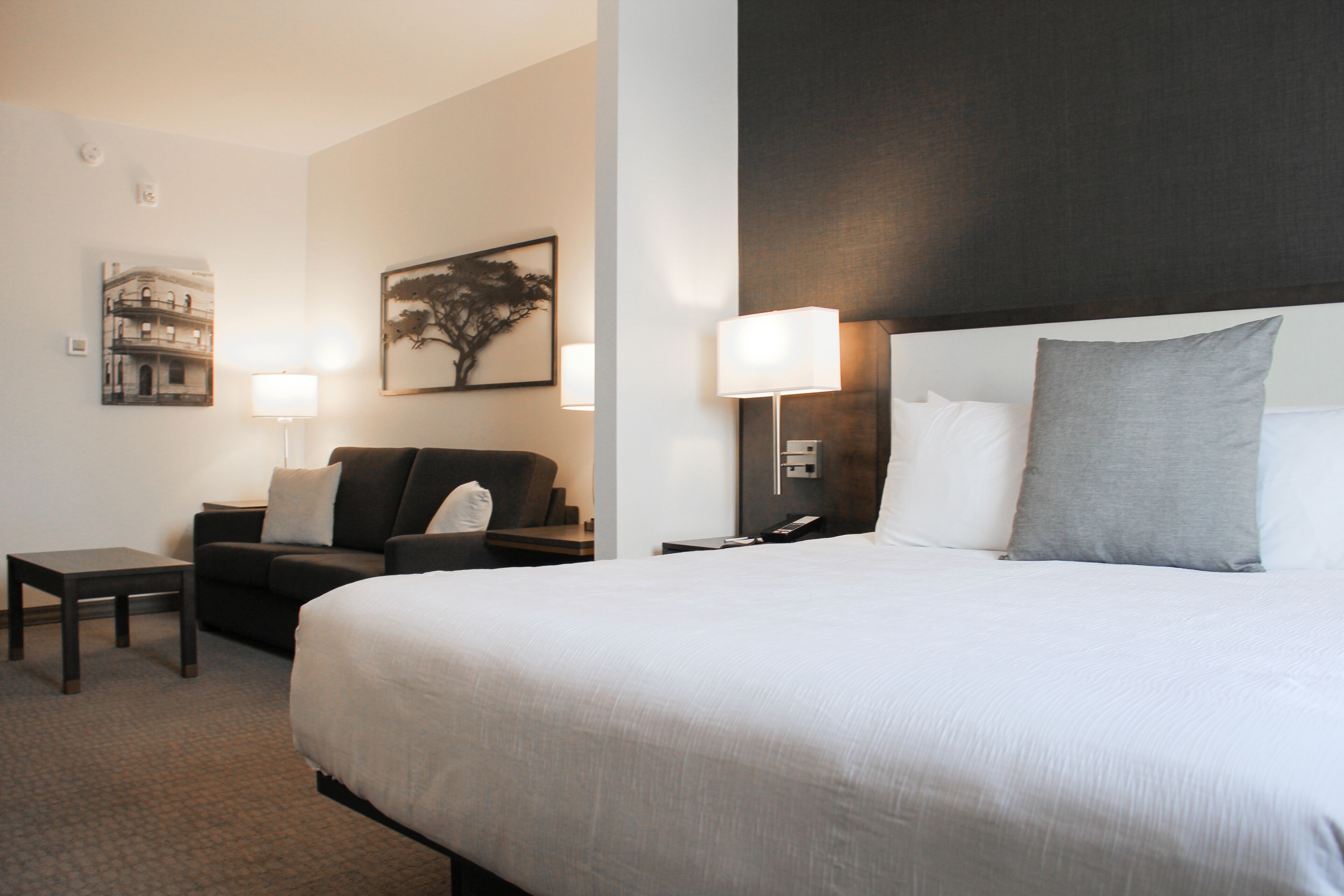 Una habitación de hotel con una cama grande, un sofá, una mesita pequeña y dos lámparas fijadas a la pared.
