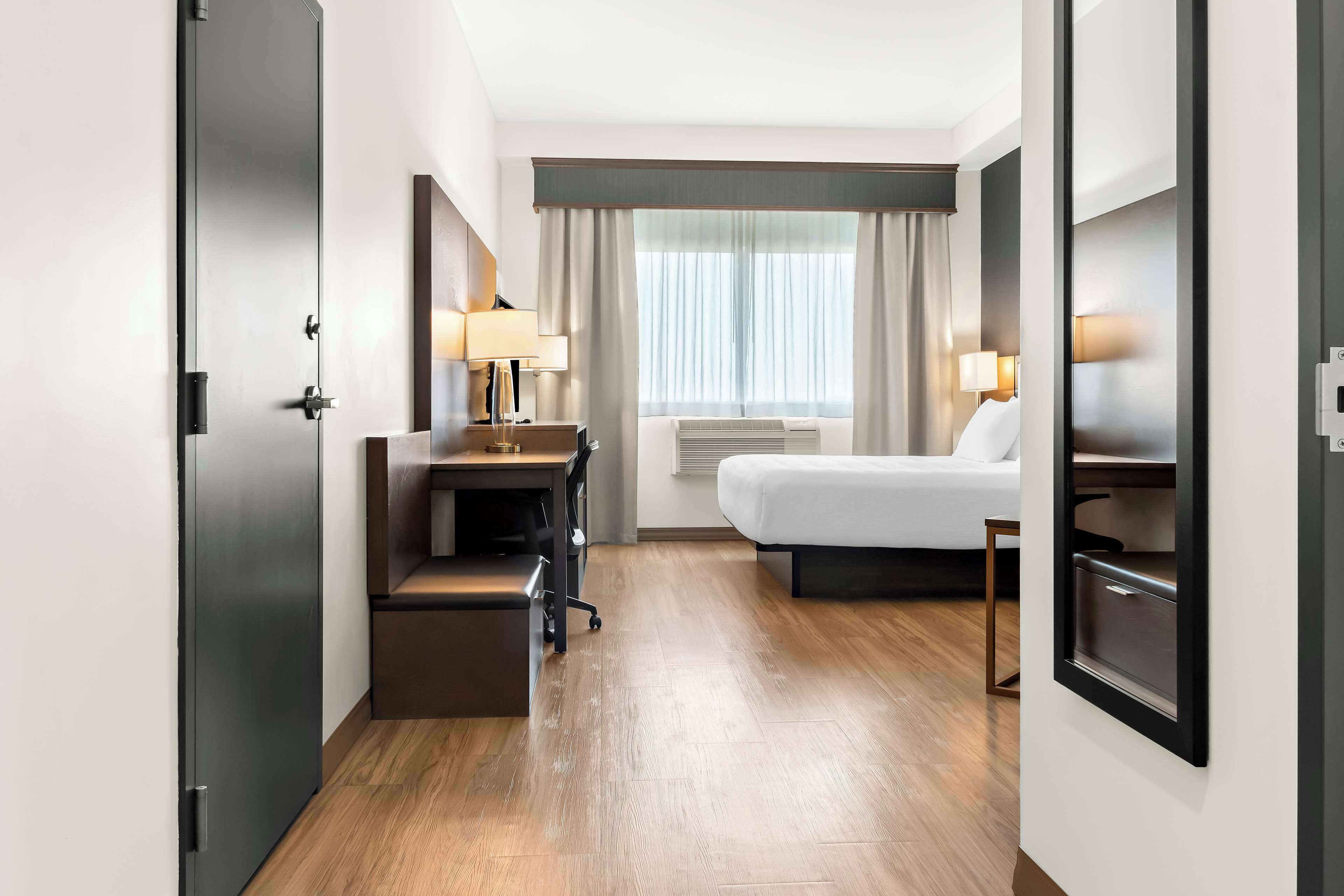 Une chambre d’hôtel avec un lit, un bureau, une chaise et une grande fenêtre avec des rideaux.